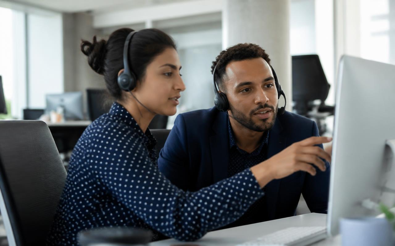 Two support specialists with headsets helping a client at a monitor